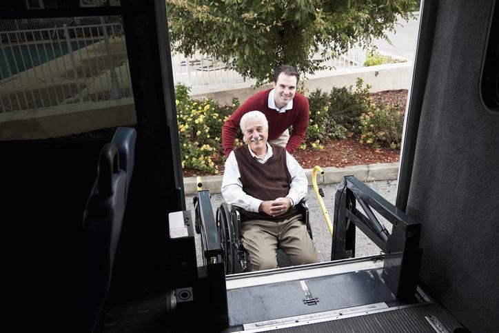 młody mężczyzna pomaga mężczyźnie na wózku wsiąść do autobusu
