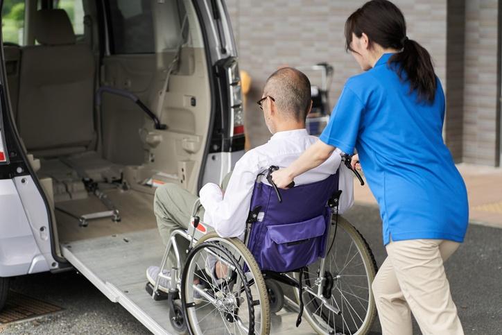 opiekunka wprowadza do samochodu osobę na wózku inwalidzkim
